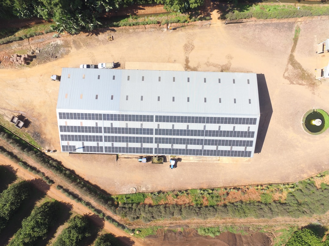 Building with solar panels, surrounded by dirt and trees.